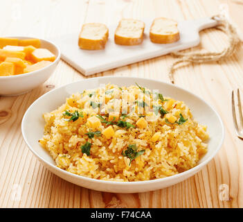 Kürbis-Risotto auf weißen Teller und Tisch aus Holz Stockfoto