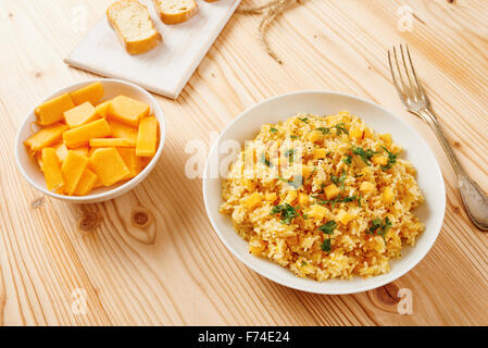 Kürbis-Risotto auf weißen Teller und Tisch aus Holz Stockfoto