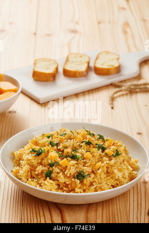 Kürbis-Risotto auf weißen Teller und Tisch aus Holz Stockfoto