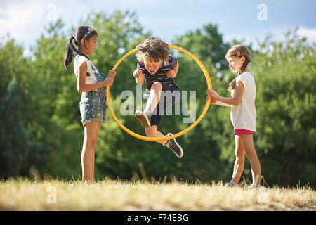 Junge springt durch Hula-Hoop während zwei Mädchen es halten Stockfoto