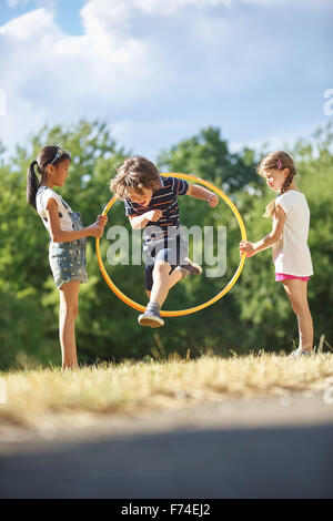 Junge im Park spielt und springt durch Hula Hoop Reifen Stockfoto