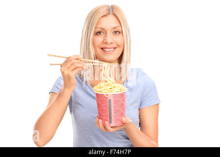 Fröhliche junge Frau essen Nudeln mit chinesischen Stäbchen und schaut in die Kamera, die isoliert auf weißem Hintergrund Stockfoto