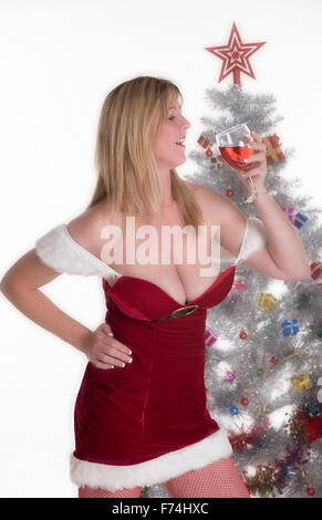 Weibliche Partei-Goer, die in einem Santa Outfit mit einem Glas Wein am Weihnachtsbaum Stockfoto