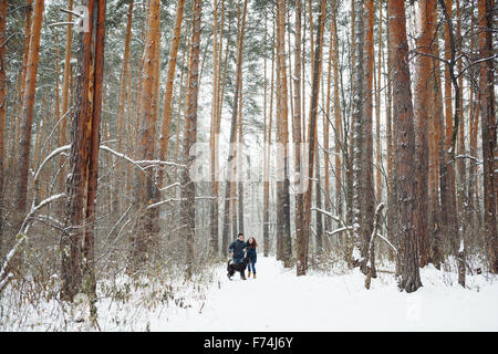 Junges Paar mit einem Hund Spaß im Winterwald an Feiertagen. Allgemeine Ansicht. Kopieren Sie Platz für Text. Stockfoto