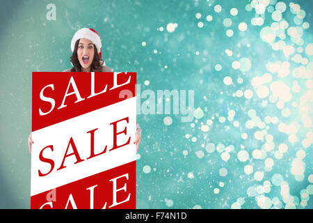 Zusammengesetztes Bild glücklich Brünette in Nikolausmütze zeigt weißes Plakat Stockfoto