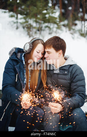 Glücklich lächelnd paar mit Urlaub Wunderkerzen feiert Weihnachten im Freien im Winterwald Stockfoto