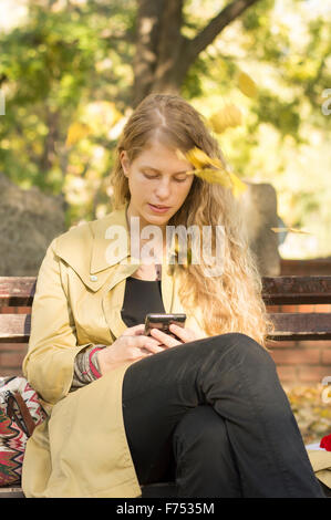 Blonde Mädchen Schreiben von Text in einem Park, während Blätter fallen Stockfoto