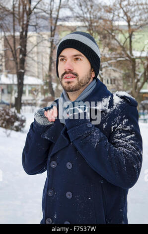 Junger Mann mit einem Mantel bedeckt mit Schnee in einem park
