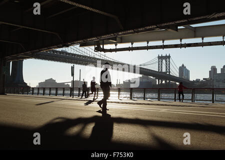 Zwei Chinatown Frauen ausüben, läuft ein Mann, eine andere geht beim betrachten die anderen entlang der East River Überführung bei Sonnenaufgang Stockfoto