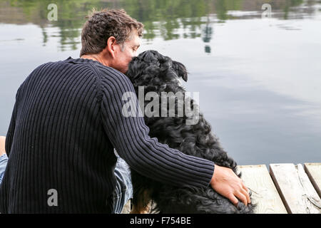 Ein Mann umarmt seinen Hund auf dem Dock am See Stockfoto