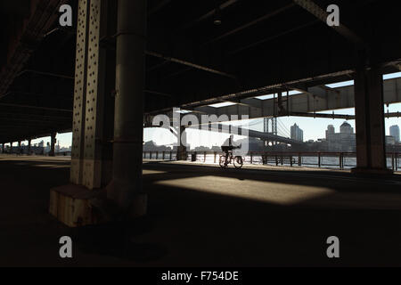 Ein Mann Zyklen entlang der East River Esplanade, New York, unter dem Franklin D. Roosevelt East River Drive Überführung bei Sonnenaufgang Stockfoto