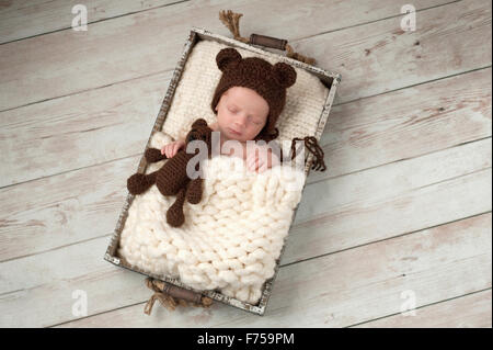 Neugeborenes Baby junge schlafen in einer Kiste und trägt eine Mütze tragen und hält einen passenden Teddybären. Stockfoto