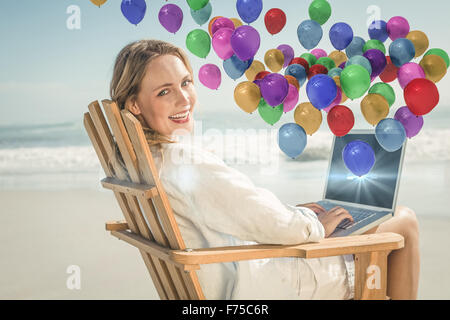 Zusammengesetztes Bild wunderschöne blonde auf Liegestuhl mit Laptop am Strand sitzen Stockfoto