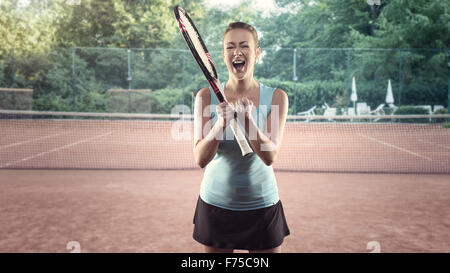 Drei Viertel Länge Porträt des sportlichen blonden Frau Holding Tennisschläger und feiern mit offenem Mund und Handbewegung auf Stockfoto