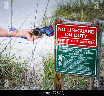 Kein Bademeister Pflicht Zeichen zusammen mit Meeresschildkröten Schutz Schild am Englewood Beach, FL, mit Frau, Sonnenbaden am Strand im bikini Stockfoto