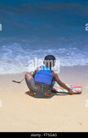 Rückansicht eines kleinen afroamerikanischen jungen in Schwimmweste mit Boogie Board betrachtet die Brandung an der Küste Stockfoto