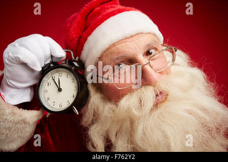 Ängstlich Santa Holding Wecker durch sein Ohr Stockfoto
