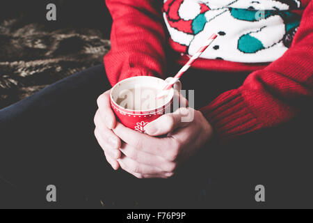 Mann trägt einen Weihnachtspullover und hält eine heiße Schokolade Stockfoto