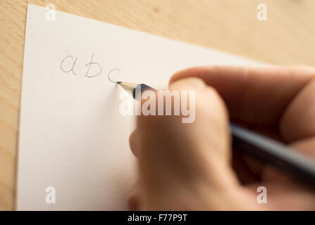 Person schreiben 'Abc' mit einem Bleistift auf weißem Papier auf ein Holzbrett oder Tischplatte gelegt. Stockfoto