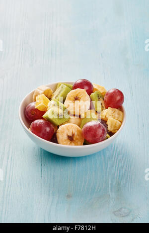 Obstsalat in Schüssel weiß auf blau Holztisch Stockfoto