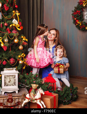 Tochter Mutter Weihnachtsbaum zu küssen. Mutter hält die jüngste Tochter in die Arme. Neues Jahr. Urlaub und Spaß. Stockfoto