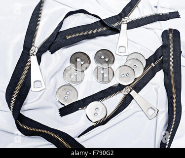 Reißverschlüsse, Knöpfe auf einen Seidenstoff liegen. Das Konzept von Handarbeiten. Mode-Design. Modehäuser. Elemente für das Nähen Stockfoto