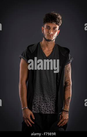 Hübscher harter junger Mann im dunklen Kapuzen-t-Shirt auf dunklem Hintergrund, Blick in die Kamera Stockfoto