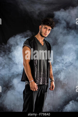 Hübscher harter junger Mann im dunklen Kapuzen-t-Shirt auf dunklem Hintergrund, Blick in die Kamera Stockfoto