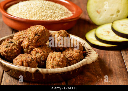 einige vegane Frikadellen in eine Steingut-Platte auf einem rustikalen Holztisch mit Gemüse im Hintergrund Stockfoto