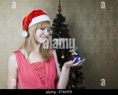 junge lächelndes Mädchen in Santas Hut und roten Kleid Weihnachtsspielzeug halten Stockfoto