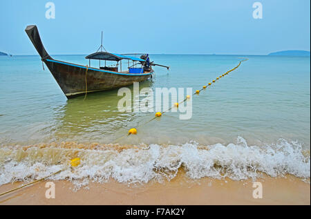 Traditionelle Thailand alte Vintage unlackiert Longtail-Boot ohne Motor in kristallklarem türkisfarbenen Wasser gekreuzt mit gelben Flora Stockfoto