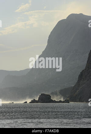 Malerische Aussicht von Sudak in Richtung Sokol (Hawk) Berg mit Fahne Spray vom stürmischen Wind über dem Meerwasser im Sonnenlicht über Stockfoto