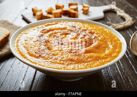 Nahaufnahme von Kürbissuppe in weiße Schüssel mit Brot Croutons auf Holztisch Stockfoto