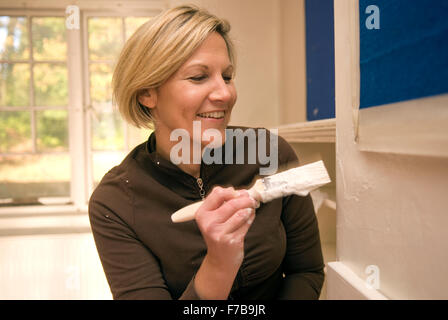 Weibliche Freiwillige mit Pinsel, Hilfe bei der Renovierung des neuen Hauses für eine lokale Pfadfindergruppe, Bordon, Hampshire, UK. Stockfoto