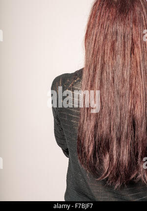 Rückansicht einer jungen Frau mit langen braunen Haaren gegen grauen Hintergrund Exemplar Stockfoto
