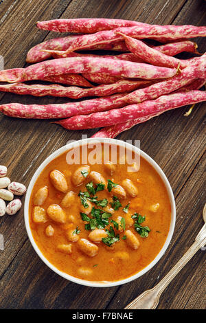 Bohnensuppe in weißen Schale umgeben von Zutaten auf Holztisch Stockfoto