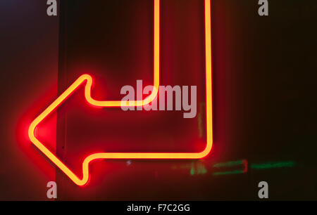 Roter Neon Pfeil nach unten und links auf dunklem Hintergrund. Stockfoto
