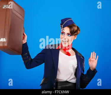 Stewardess mit Gesicht Kunst hält Koffer. Junge attraktive Mädchen in einem blauen Anzug Flugbegleiter. Lufttransport. Service. Stockfoto