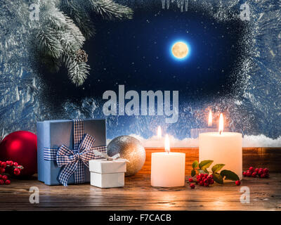 Weihnachtsgeschenke mit brennenden Kerze auf der Fensterbank mit Muster Frost. Stockfoto