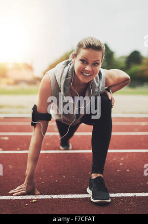 Junge blonde Sportlerin Blick in die Kamera beim stretching auf Stadion vor laufen, Musik hören Stockfoto