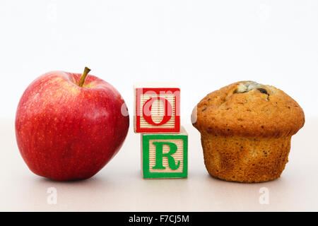 Rosy Red Apple und einen Muffin Kuchen mit Word oder im Schreiben Blöcke auf einer Tischplatte Wahl der gesund oder ungesund essen Konzept veranschaulicht gut Essen. Stockfoto