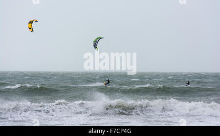 Kiter und Surfer reiten weiß schäumende Wellen in stürmischen Winter Wetter in Boscombe, Bournemouth, Dorset, Großbritannien Stockfoto