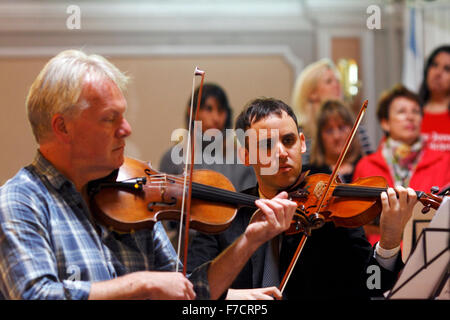 Zwei Männer spielen Violine mit einem Chor im Hintergrund. Chor Proben Stockfoto