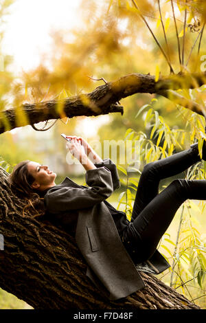 Oung Frau ruht auf den Baum mit Handy Stockfoto