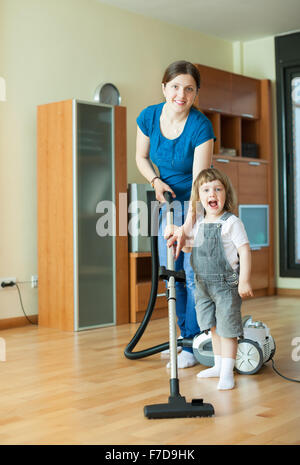 Frau lehrt Mädchen, den Staubsauger zu Hause zu verwenden Stockfoto