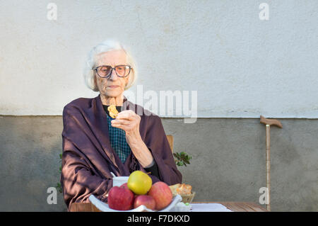 90 Jahre alte Oma mit einem Snack im Hinterhof Stockfoto