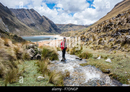 Frau, trekking und Wildbach am See Quengococha in Bergen in der Nähe von Cajabamba in Peru Stockfoto