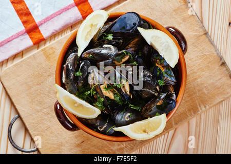 Muscheln in einem Topf auf dem Schneidebrett, Zitronen, Tischdecke auf Holztisch Stockfoto