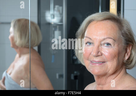 Attraktive blonde ältere Frau stehen eingewickelt in ein Handtuch im Badezimmer, Nahaufnahme Portrait von ihr Gesicht mit ihrem Körper-Reflexion Stockfoto