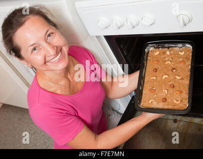 Reife Frau Bräter in Ofen Teig aufsetzen. Eines der Stadien des Kochens des Honigkuchen.  Serien ansehen Stockfoto